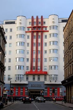 cars are parked in front of a tall white building with red trim on the side