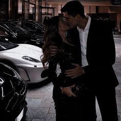 a man and woman kissing in front of parked cars