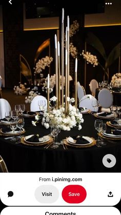 a black table topped with lots of white flowers and gold place settings next to tall candles