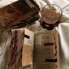 an open book sitting on top of a bed next to a glass filled with liquid