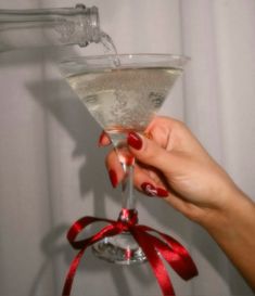 a woman's hand holding a martini glass with white wine and red ribbon around it