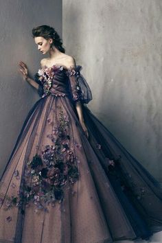 a woman in a dress with flowers on it standing against a wall and looking off to the side