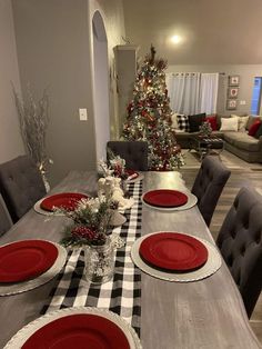 a dining room table set for christmas with red plates and place settings on it,