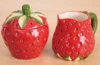 two ceramic strawberry mugs sitting on top of a wooden table