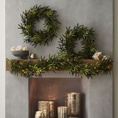 two wreaths are hanging on the mantle above candles