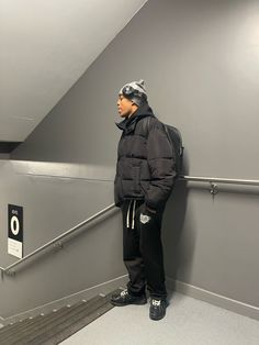 a man in a black jacket and hat standing on a stair case with his back to the camera