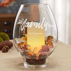 a glass vase with the words family on it sitting on a table next to pine cones and other decorations