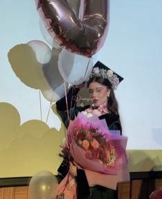 a woman holding flowers and balloons in front of a screen