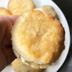 a hand holding a biscuit in front of some other biscuits on a white plate