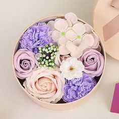 a pink box filled with purple and white flowers next to a pink gift bag on top of a table