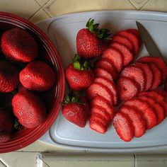 strawberries are cut up and placed on a cutting board next to a bowl of strawberries