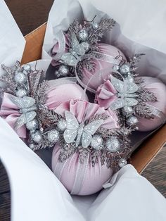 three pink christmas ornaments in a box on a wooden table with white paper and silver ribbon