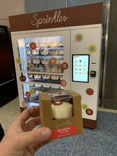 a person holding up a box with some food inside of it in front of a vending machine