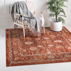 an orange rug with a chair, potted plant and blanket on it in front of a white wall