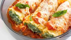 a glass bowl filled with lasagna covered in cheese and spinach leafy garnish