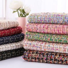 a stack of multicolored blankets sitting next to a vase with flowers in it