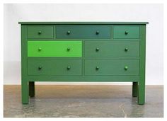 a green dresser sitting on top of a floor next to a white wall in a room