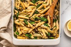 a casserole dish filled with pasta, spinach and mushrooms next to a wooden spoon