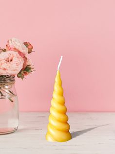 a yellow candle sitting next to a vase filled with pink flowers on top of a table