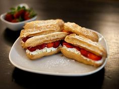 two sandwiches are sitting on a plate with strawberries in the bowl next to it