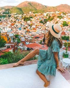 a woman sitting on top of a building next to a lush green hillside