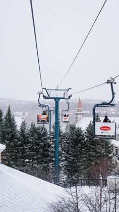 a ski lift with two people on it going over the snow covered ground and buildings in the background