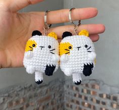 two crocheted keychains with cats on them are being held by someone's hand