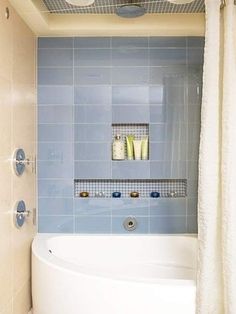 a bath tub sitting next to a shower curtain in a bathroom with blue tiles on the walls