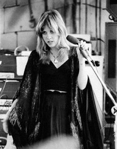 a woman in a black dress holding a microphone and standing next to a recording studio