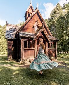 a woman in a blue dress is walking towards a wooden church with a steeple