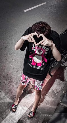 a person making a heart shape with their hands while standing on the side of a road