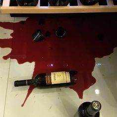 a bottle of wine sitting on top of a counter covered in red liquid next to bottles