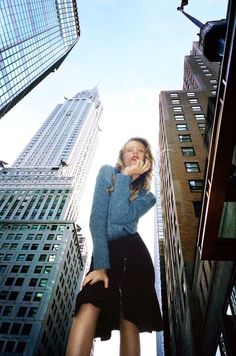 a woman standing in the middle of tall buildings with her hands on her hips and looking up at the sky