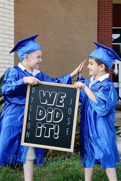 two young boys in graduation gowns are holding a sign