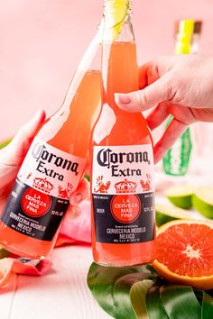 two bottles of corona extra on a table with grapefruits and orange slices