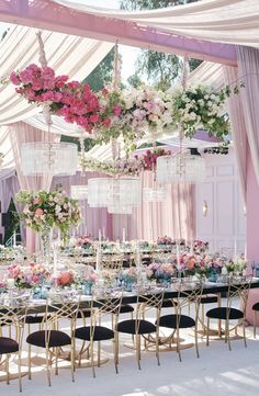 an outdoor wedding reception with pink and white flowers hanging from the ceiling, chandeliers and tables