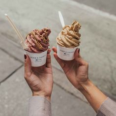 two people holding up ice cream cones with toppings in their hands on the sidewalk