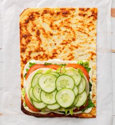 a sandwich with cucumber and tomato slices on it, sitting on top of a piece of paper