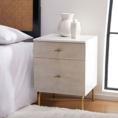 a nightstand with two vases on top of it next to a bed and window