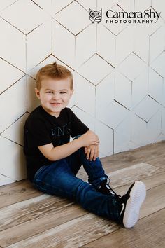 a young boy sitting on the floor in front of a white wall with he's legs crossed