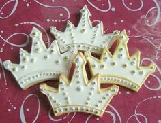 three decorated cookies in the shape of crowns on a pink tablecloth with swirls