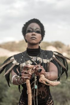 a woman with an animal headdress holding a stick and snake skin on her hands