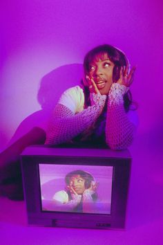 a woman sitting on top of a tv next to a purple wall