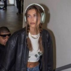 a woman wearing headphones walking through an airport terminal with another man in the background