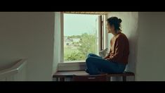 a woman sitting on a window sill reading a book