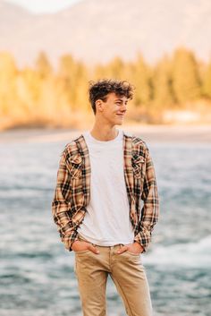 a young man standing on the edge of a cliff by the water with his hands in his pockets