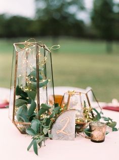 the table is set up with candles, greenery and glass vases on it