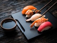 sushi on a black plate with chopsticks and sauce in front of it