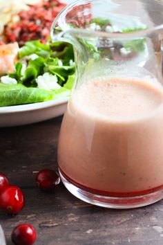 a glass pitcher filled with liquid sitting next to a plate of salad and cherries