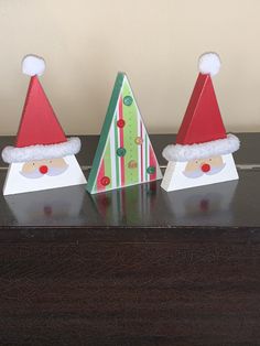 three paper santa hats on top of a wooden table next to a christmas card holder